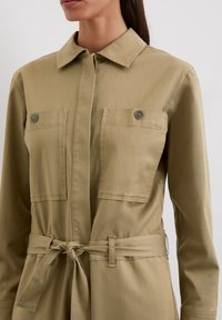 Kaki Utility-Kleid mit Kragen, zwei Brusttaschen, einem Bindegürtel und einem glatten, leichten Stoff. Mit Knopfdetails.