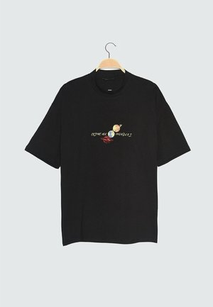 T-shirt nera a maniche corte su una gruccia di legno con un design a tema spazio e il testo "Cosmic Age Invaders" sul petto.