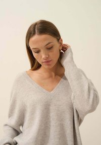 Lichtgrijze, langarmige v-hals trui met een losvallende pasvorm en geribbelde textuur. Beschikt over brede mouwen en subtiele stiksels.