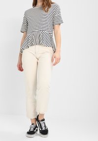 Top peplum a rayas en blanco y negro, combinado con jeans de mezclilla crema. La modelo lleva deportivas negras con acentos blancos.