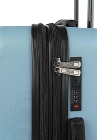 Maleta de hard-shell en azul claro con acabado texturizado, que cuenta con dos cremalleras negras, una cerradura de combinación y un mango extensible.