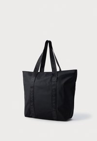 Czarna torba typu tote wykonana z lekkiego nylonu, z teksturowanymi ramiączkami z wytłoczonym logo, prostokątny kształt i minimalistyczny design.