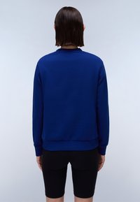 Marineblauwe trui met lange mouwen, ronde halslijn, ribbelmanchetten en onderrand, gecombineerd met zwarte shorts, gezien vanaf de achterkant.