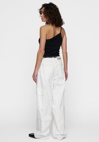 Zwarte asymmetrische tanktop gecombineerd met ruime, witte cargobroek met meerdere zakken en een gestructureerde tailleband.