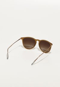 Ochelari de soare maro cu formă cat-eye, lentile cu degradé și brațe subțiri din metal, având vârfuri gri și o finisare mată pe exteriorul ramei.
