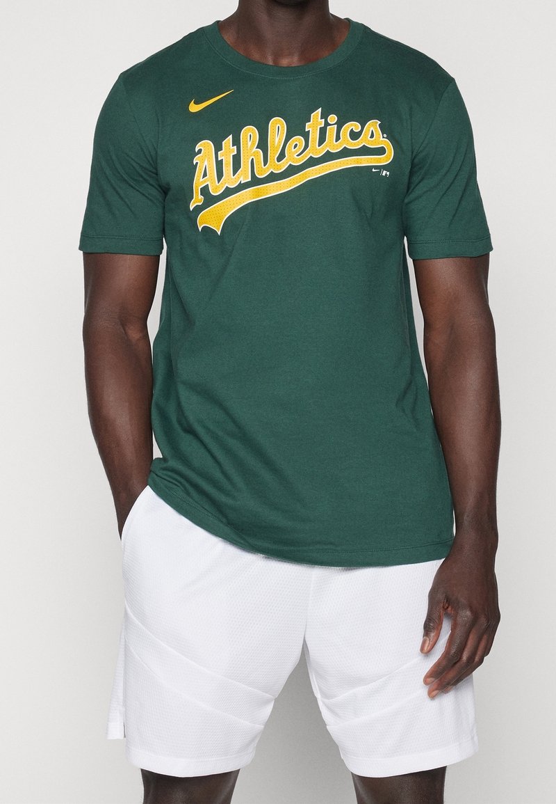 Mørkegrøn bomuld t-shirt med gul "Athletics" tekst, rund hals, korte ærmer, matchende med hvide mesh shorts. Nike-logo på brystet.