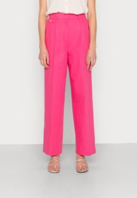 Calças largas fúcsia com cintura alta, pregas frontais e detalhe de botão. Tecido suave e bainha curta. Combinadas com sandálias de tiras.