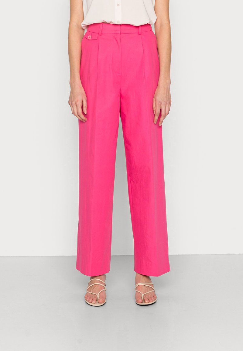 Calças largas fúcsia com cintura alta, pregas frontais e detalhe de botão. Tecido suave e bainha curta. Combinadas com sandálias de tiras.