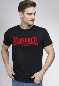 Fekete pamut póló, piros "Lonsdale London" grafikával elöl. Rövid ujjú, kerek nyakú és laza szabású. Egyszerű dizájn.