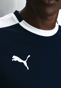 Gros plan d'une personne portant un maillot de sport Puma bleu marine avec un col blanc et un logo sur la poitrine.