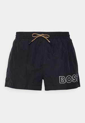 Shorts de bain noirs avec une taille élastique, cordon de serrage ajustable en beige et logo "BOSS" blanc sur le côté gauche. Texture de tissu lisse.