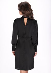 Abito in satin nero con maniche a sbuffo lunghe, vita aderente e dettaglio a forma di chiave sulla schiena. Texture liscia, lunghezza fino al ginocchio e chiusura con zip nascosta.