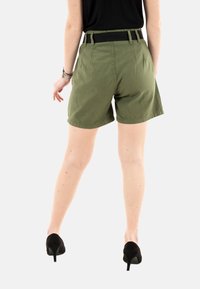 Pantalones cortos de algodón verde con cintura alta, cinturas y un diseño sólido. Llevados con tacones altos negros, mostrando una textura suave.