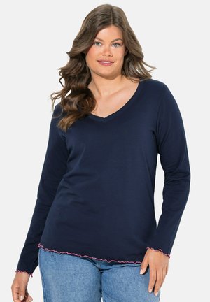 Marineblauwe longsleeve top met een V-hals ontwerp en een roze gerimpelde zoom en mouwmanchetten; gemaakt van zachte stof. Geshowd met lichtblauwe jeans.