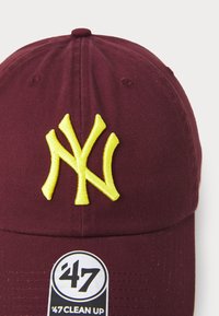 Maroon kapa za bejzbol s žutim izvezenim 'NY' logom, napravljena od pamuka. Uključuje crnu oznaku '47 CLEAN UP'.