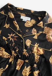 Set de pijamale negre cu un motiv auriu reprezentând mâini, chipuri și obiecte, cu margini galbene, talie cu șnur și sistem de închidere cu nasturi.