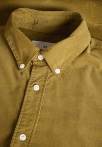 Camicia di velluto a coste verde oliva con colletto abbottonato e bottoni bianchi, caratterizzata da rigature verticali e una trama liscia.