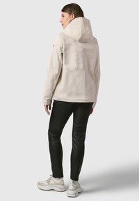 Lichtbeige hooded jack met een gestructureerde stof, met een rechte snit, kangoeroezak, en gecombineerd met zwarte strakke broek en sportieve schoenen.