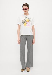 T-shirt bianca con grafica colorata di limone e foglie, abbinata a pantaloni a zampa d'elefante a righe bianche e nere e scarpe slip-on beige.
