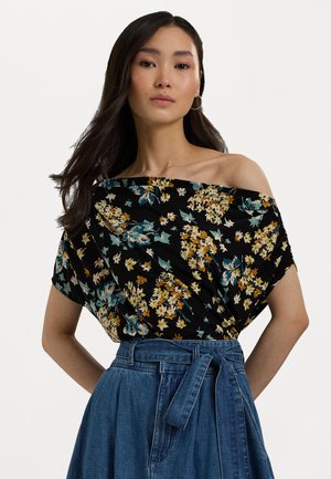 Bloemrijke off-shoulder top met een zwarte achtergrond, voorzien van gele, blauwe en groene bloemen. Gecombineerd met een hoge taille spijkerrok.