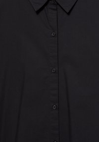 Camicia nera con colletto, realizzata in tessuto morbido, caratterizzata da una serie di bottoni neri abbinati lungo la parte anteriore.