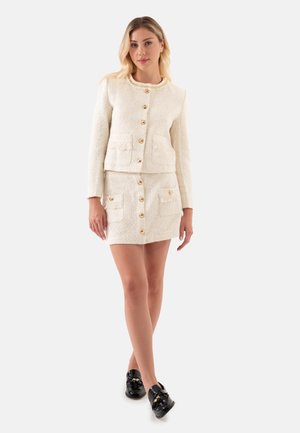 Witte gebreide jas met structuur en gouden knopen, voorzien van twee voorzakken, gecombineerd met een bijpassende mini rok met knoopdetails en zakken.