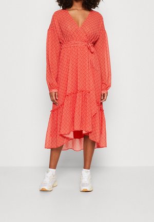 Vestido envolvente de estampado rojo con mangas largas, cinturilla atada y falda acampanada. Combinado con zapatillas blancas que cuentan con un diseño de dobladillo en capas.