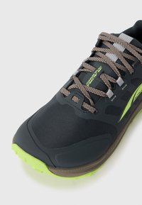 Scarpa sportiva nera e verde neon con lacci marroni a motivo e etichetta "Lone Peak Waterproof" sulla linguetta, su sfondo bianco.