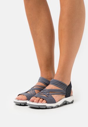 Grey and white sandals with woven straps and a cushioned sole. Features a padded ankle and rubber outsole for grip. Open-toe design.
