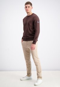 Bruine lange mouwen sweatshirt met een ronde halslijn en geribde manchetten, gecombineerd met beige slim-fit broek en witte sneakers.
