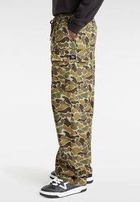 Camouflage cargobroek in groen, bruin en tan. Voorzien van een elastische tailleband, zijzakken en een relaxte pasvorm. Gecombineerd met zwarte sneakers.