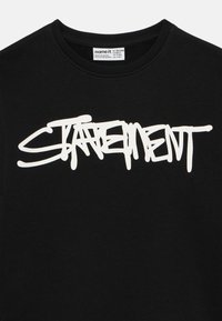 Felpa nera in tessuto morbido con scritta audace in stile graffiti bianco "STATEMENT" sulla parte anteriore.