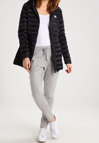 Svart puffjacka med huva och dragkedja, vit logotyp. Grå joggers med dragsko, slim fit. Vita sneakers. Slät tyg, avslappnad stil.