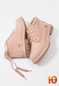 Różowe zamszowe botki za kostkę posiadają metaliczny złoty akcent na obcasie, wytrzymałą podeszwę oraz satynowe sznurówki. Na boku widoczne jest logo Timberland.