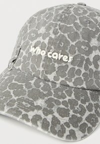 Γκρι καπέλο μπέιζμπολ με λεοπάρ μοτίβο, λευκή κεντημένη επιγραφή «who cares» και μικρό μεταλλικό κρίκο στη μία πλευρά.