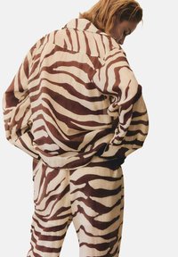 Hnědo-krémová pruhovaná oversize bunda a kalhoty, které nabízejí volný střih, měkkou tkaninu a výjimečný vzor zebra.