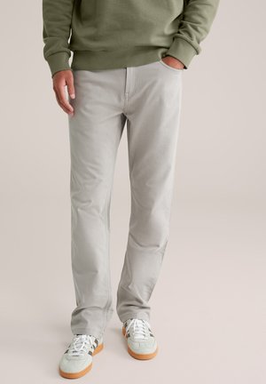 Lichtgrijze rechte broek van een katoenmix, met zijzakken en subtiele stikdetails, gecombineerd met groene en bruine sneakers.