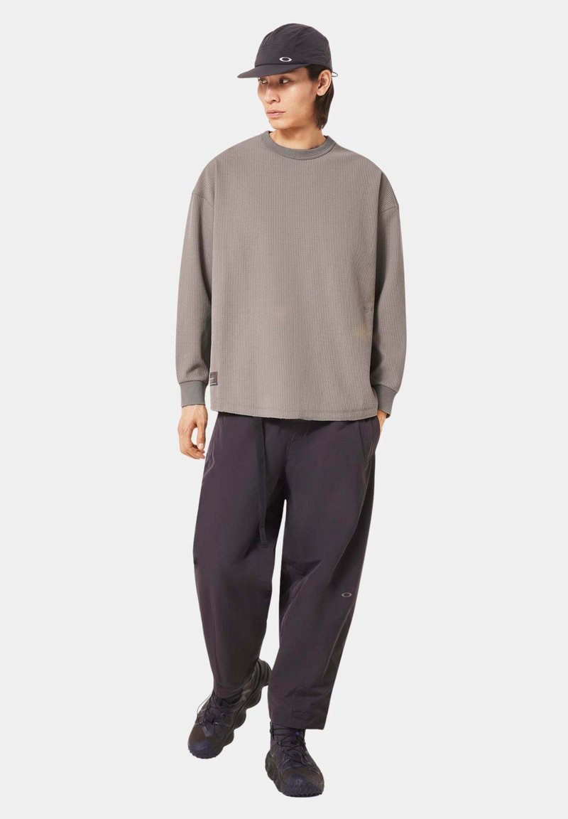 Gray long-sleeve textured shirt with a round neck, paired with loose-fitting black pants. Black cap and dark footwear complete the look.