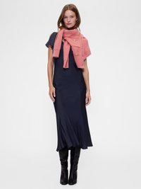 Rochie midi bleu marin cu un tiv evazat, purtată cu un șal texturat coral din tricot, cu accente aurii. Modelul poartă cizme negre până la genunchi.