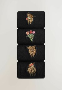 Četiri crne presavijene čarape složene okomito, svaka s drugačijim izvezenim motivom: dvije koze, buket tulpana i koza s šeširom.