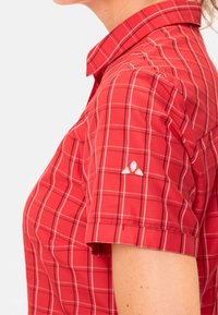 Camicia a maniche corte a quadri rossi con colletto a punta, un logo ricamato discreto sulla spalla e un tessuto morbido e texture.