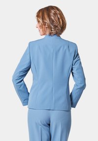 Lichtblauwe op maat gemaakte blazer met een getailleerd ontwerp, een zachte textuur, gestructureerde schouders en een hoge kraag, gezien vanuit de achterkant.