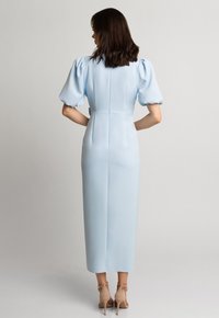 Jasnoniebieska sukienka do kolan z bufkowymi rękawami, dopasowanym bodicem i subtelnym zamkiem błyskawicznym z tyłu; połączona z beżowymi sandałami na wysokim obcasie.