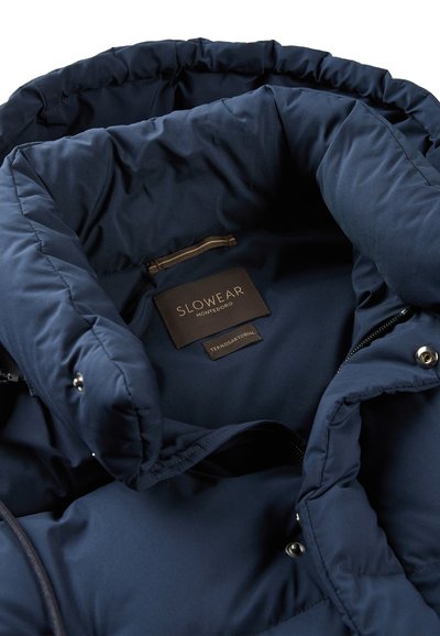 Interno di una giacca a vento blu navy con una texture liscia, caratterizzato da un'etichetta che legge "SLOWEAR MONTEDORO" e una tasca con zip.