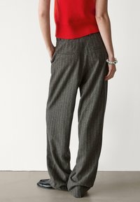 Pantalon gris à fines rayures avec une coupe ample, doté de deux poches arrière. Le tissu semble texturé. Associé à un haut en laine rouge.