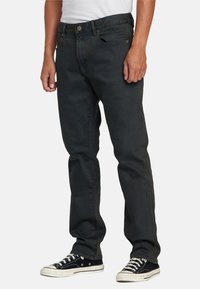 Jeans de mezclilla oscura con un corte relajado, con cierre de botón, cinco bolsillos y costuras amarillas contrastantes. Combinados con zapatillas negras.