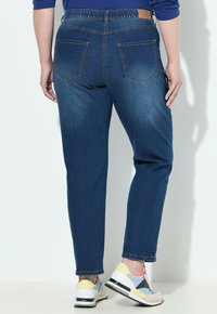 Blaue Jeans aus Denim mit einem dehnbaren Bund, ausgestattet mit zwei Gesäßtaschen und einer lässigen Passform. Kombiniert mit mehrfarbigen Sportschuhen.