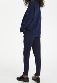 Mörkblå stickad tröja med avslappnad passform, kombinerad med mörkblå avsmalnande byxor och glänsande svarta snörskor.