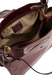 Bordeaux læderhåndtaske med en blank finish, der har en beige stofindvendig, en lynlåslomme og to bærehåndtag.