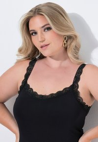 Černá košilka s krajkovým lemem na výstřihu a ramínkách. Měkká, přiléhavá látka s nastavitelnými ramínky. Průhledné pozadí.